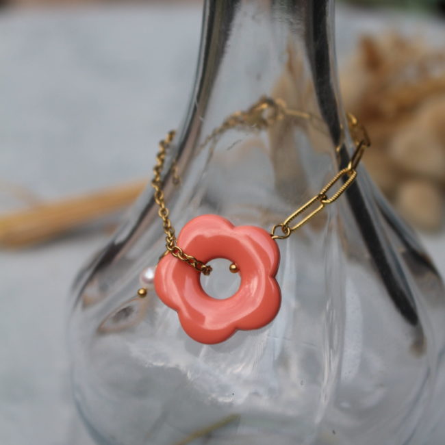 Bracelet fleur asymétrique. D'un côté, une chaine dorée à maillons ovales, de l'autre une chaine dorée à petits maillons ronds. Au centre, une belle fleur couleur corail et sa perle nacrée.